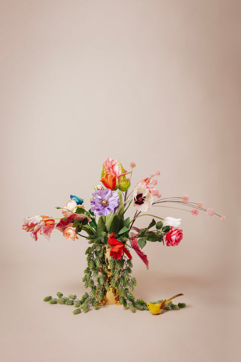 Boeket van hoogwaardige kunstbloemen, waaronder rode, roze en lavendelkleurige bloesems met groen bladwerk, gepresenteerd in een gouden vaas, een duurzaam en onderhoudsvrij alternatief voor verse bloemen.