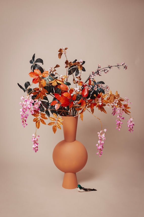 Odette's kunstbloemenarrangement in een terracotta vaas, een mix van herfsttinten en roze bloesems, creëert een warme en uitnodigende sfeer voor elk interieur