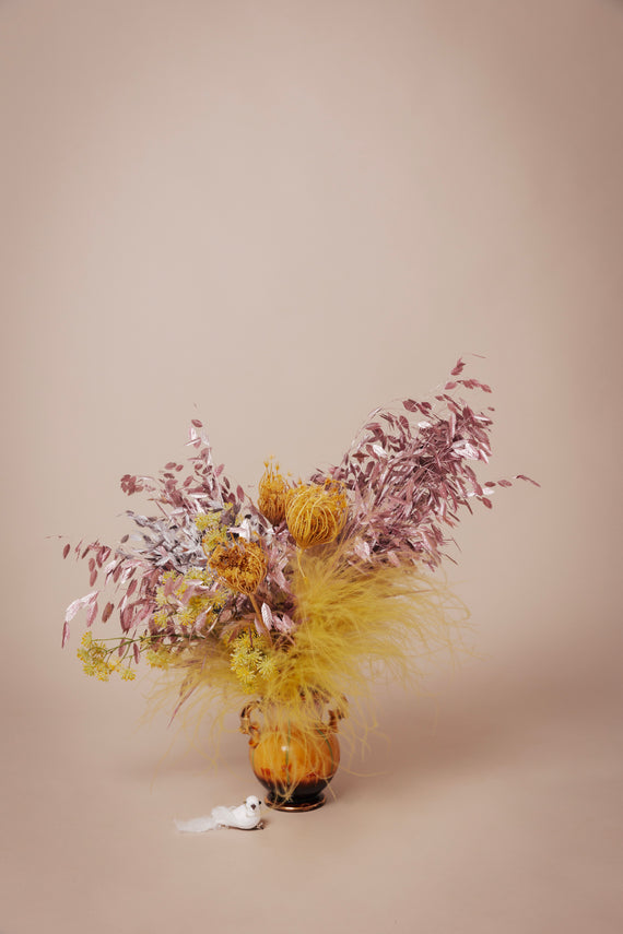 Een weelderig boeket van luxe kunstbloemen, met een diversiteit aan texturen en kleuren waaronder geel en lila, zorgvuldig gearrangeerd in een sierlijke vaas als decoratie klein boeket