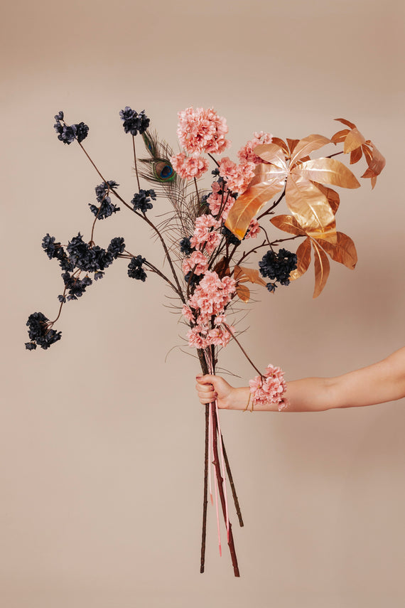Een boeket van luxe zijden bloemen in roze en blauw, verrijkt met gouden bladeren en een opvallende pauwenveer, perfect voor een stijlvolle tafeldecoratie